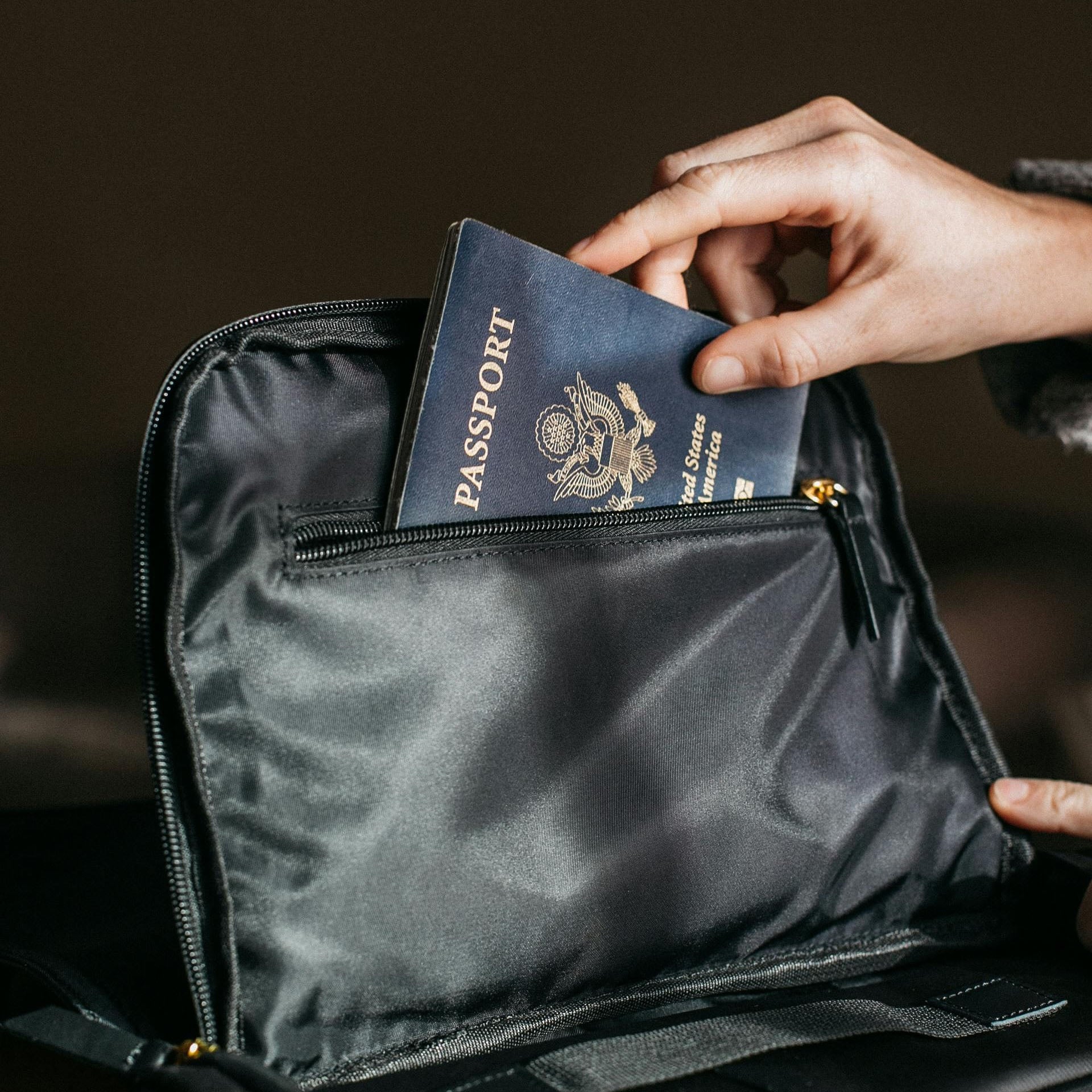 Hand placing a U.S. passport into a black travel bag, symbolizing travel restrictions and legal concerns.